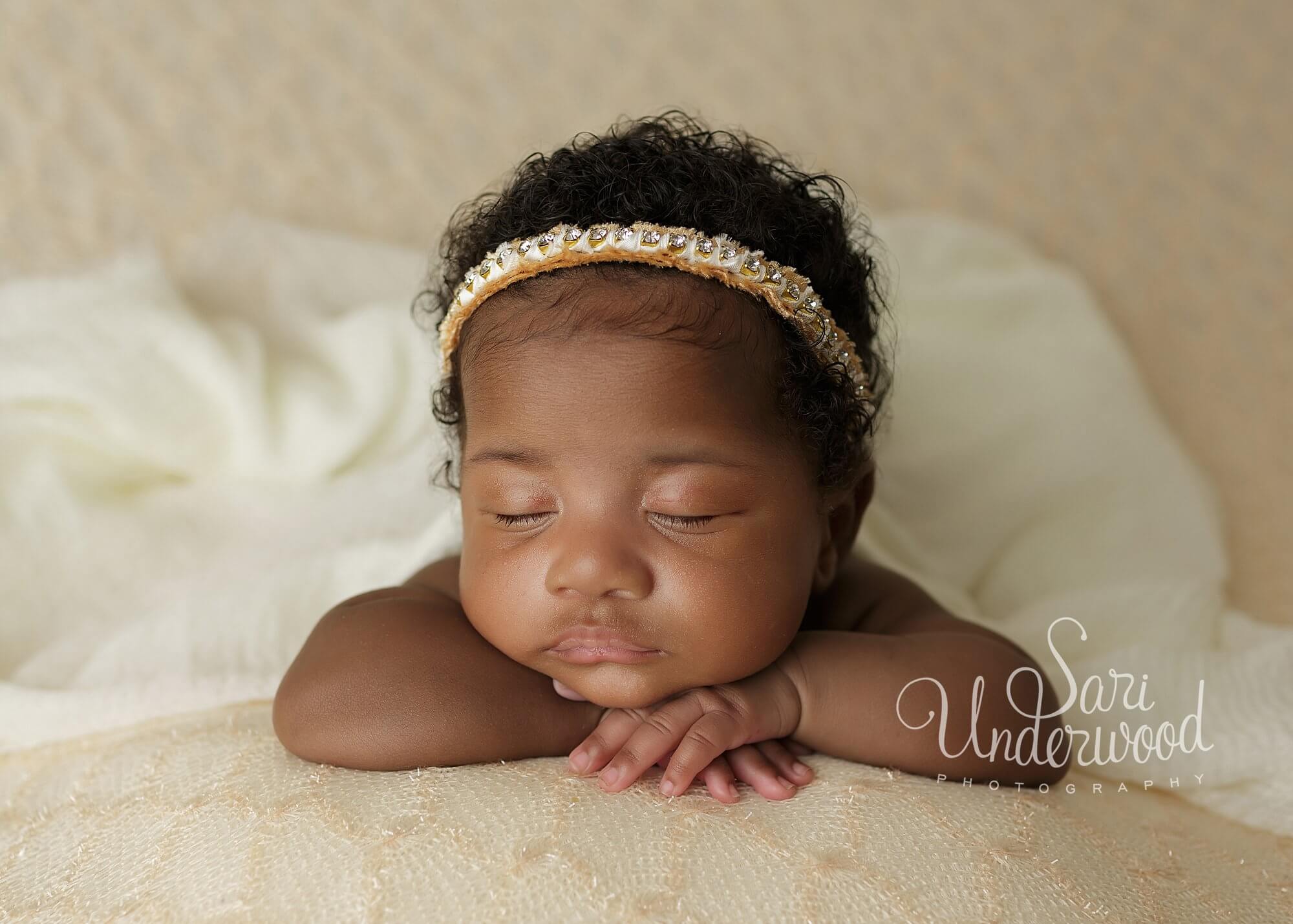 black baby girl with head resting on hands adorned in gold headband